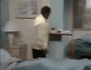 a man is standing in a room next to a bed and a table .
