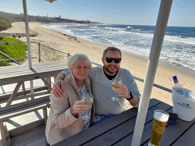 a man and a woman are sitting at a picnic table with a bottle of blue point beer
