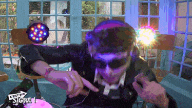 a man wearing sunglasses and headphones is pointing at something in front of a sign that says " c'est bon signe "