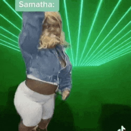 a woman in a denim jacket and white shorts is dancing in a green room .