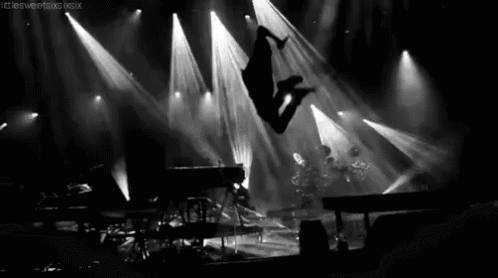 a black and white photo of a person jumping in the air on a stage at a concert .