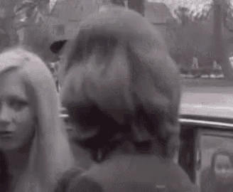 a black and white photo of a group of women standing next to each other in front of a car .