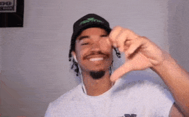 a man wearing a hat and ear buds is making a heart shape with his hands .