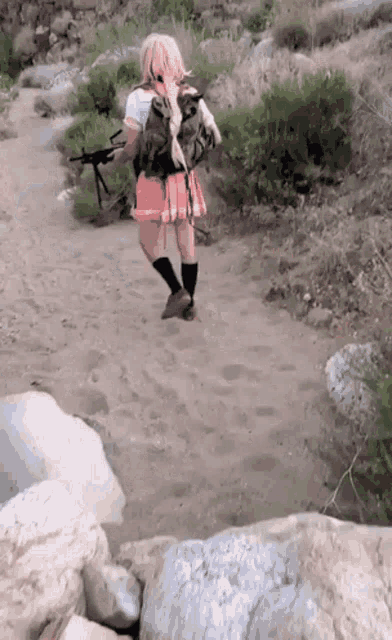 a girl in a skirt is walking down a dirt path carrying a gun