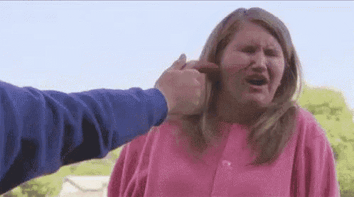 a woman in a pink sweater is being punched in the face by a man in a blue sweater .