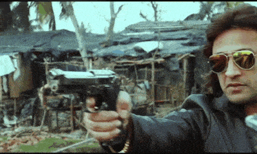 a man wearing sunglasses and a leather jacket is pointing a gun
