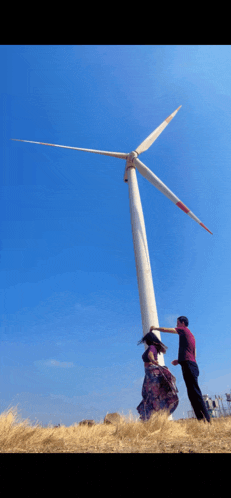 a man and a woman are standing in front of a large windmill