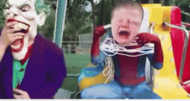 a baby in a superhero costume is crying next to a joker puppet .