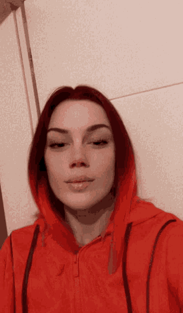 a woman with red hair and a red hoodie takes a selfie