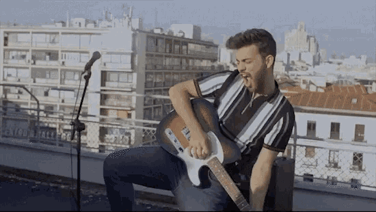 a man is singing into a microphone while playing a guitar on a balcony
