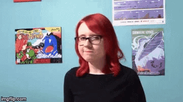 a woman with red hair and glasses is standing in front of a wall with posters on it including one that says submarine voyage on it