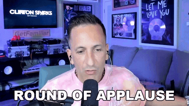 a man sitting in front of a microphone with the words round of applause behind him