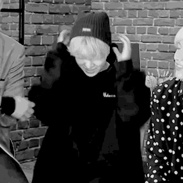 a group of people are standing in front of a brick wall . one of the people is wearing a beanie .