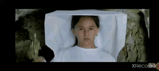 a young girl is laying in a coffin with a white cloth over her head .