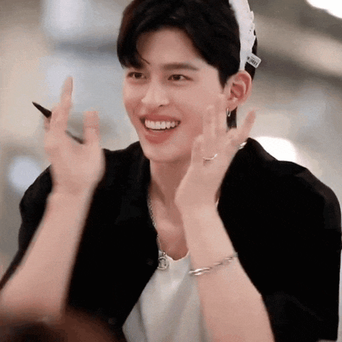 a young man wearing a hat and a bracelet is smiling and making a peace sign .