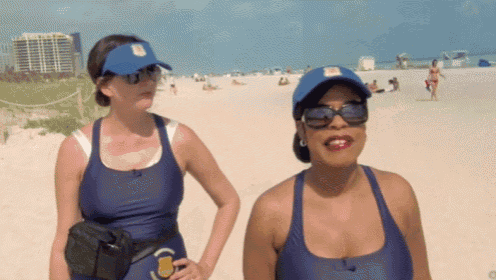 two women wearing blue swimsuits and blue hats stand on a beach .