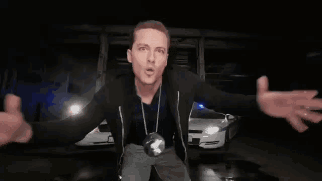 a man is standing in front of a car with his arms outstretched in a parking garage .