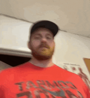 a man with a beard and a hat is wearing a red shirt and a black hat .