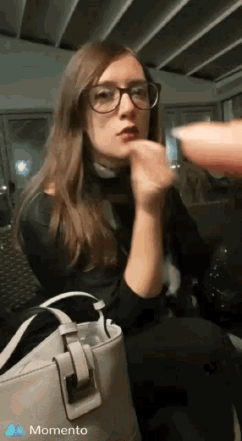 a woman wearing glasses and a purse has a momento logo on the bottom