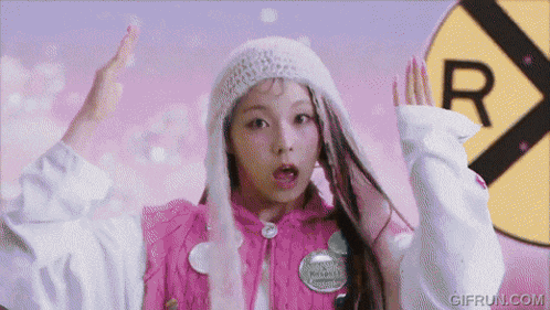 a girl wearing a pink sweater and a white hat is standing in front of a yellow sign that says r.