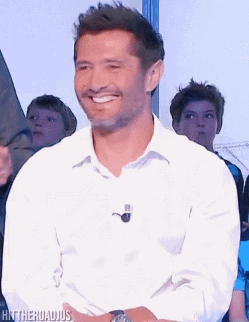 a man in a white shirt is smiling in front of a group of children with the words hntheroadjus below him