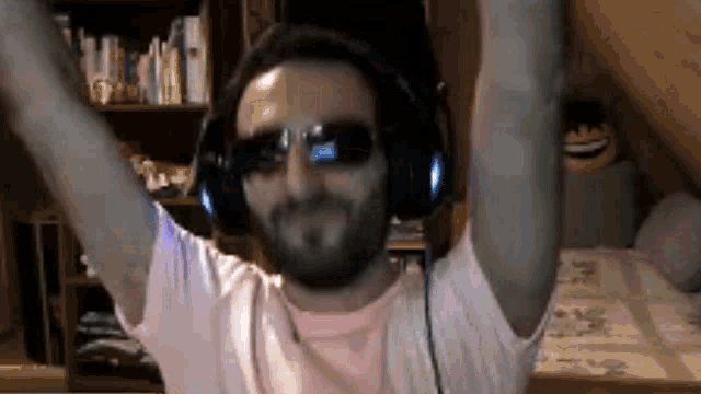 a man with a beard wearing headphones and sunglasses is dancing with his arms in the air .