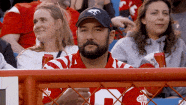 a man with a beard wearing a hat with a horse on it is sitting in a crowd of people