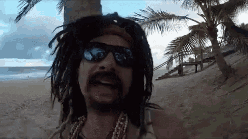 a man with dreadlocks and sunglasses is standing on the beach .