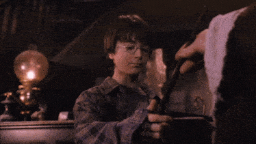 a young boy in a plaid shirt is holding a wand in a dark room