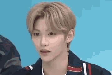 a young man with blonde hair and earrings is looking at the camera .