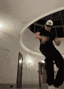a man wearing a black shirt and a white nike hat is dancing in a room
