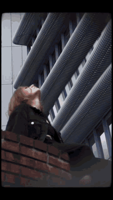 a woman is sitting on a brick wall looking up at a building