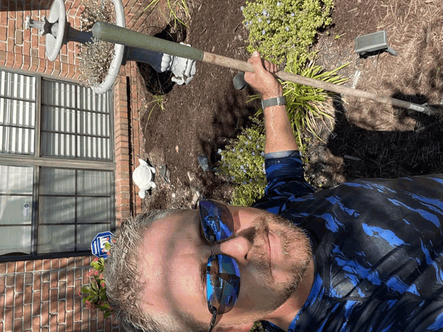 a man wearing sunglasses and a blue shirt is standing in a garden