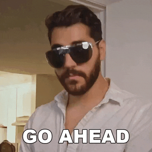 a man with a beard wearing sunglasses and a white shirt says go ahead