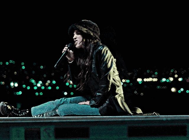 a woman is singing into a microphone while sitting on a ledge