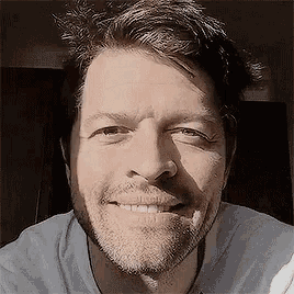a man with a beard is smiling for the camera while wearing a white shirt .