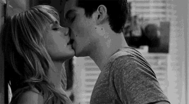 a black and white photo of a man and a woman kissing against a wall .