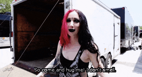 a woman with red and black hair is standing in front of a trailer and says so come and hug me i don t smell