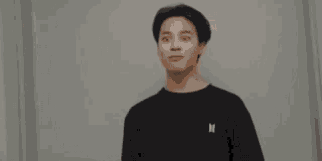 a man in a black sweater is standing in front of a mirror .