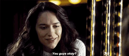 a woman in a white sweater is smiling and talking to a man in a dark room .