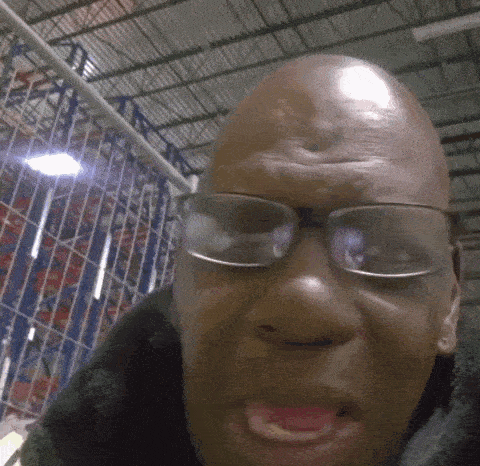 a bald man wearing glasses is making a funny face in a warehouse