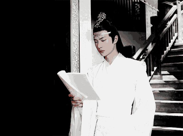 a man in a white robe is reading a book next to stairs