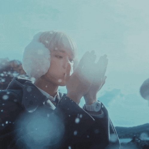 a person wearing ear muffs and a watch is blowing snow in the air