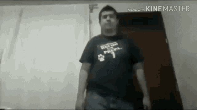 a man wearing a black shirt with a paw print on it is standing in a doorway .