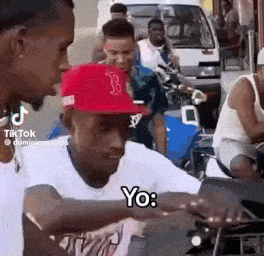 a man wearing a red hat is talking to another man on a motorcycle .