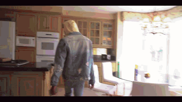 a person wearing a denim jacket is walking through a kitchen