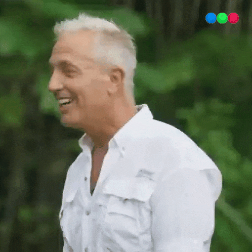 a man in a white shirt is smiling in front of a green bush