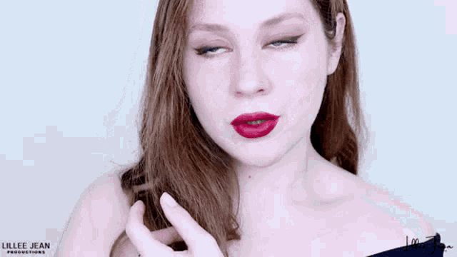 a woman wearing red lipstick and a black off the shoulder top is pointing at her hair .