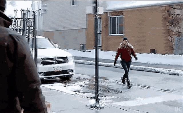 a woman crosses the street in front of a white dodge