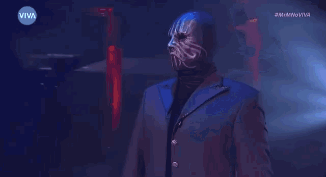 a man in a suit and mask is dancing in a dark room with a viva logo in the background